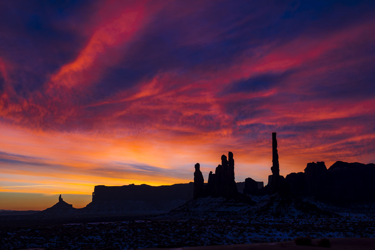 The first colors of sunrise, a combination of deep gold, red and blue, fill the sky over the Totem formation at Monument Valley...