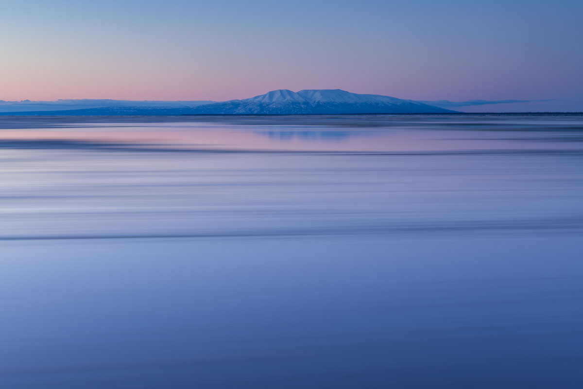 Mt. Susitna looms in the background as the winter tides zoom by in a long exposure at sunset.