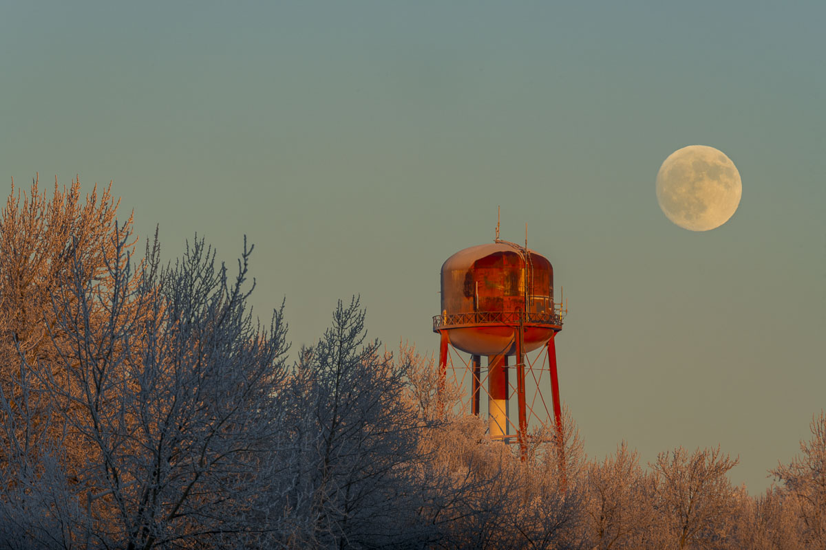 The full moon rises past an old water tower in the Government Hill neighborhood of Anchorage during a frosty winter.