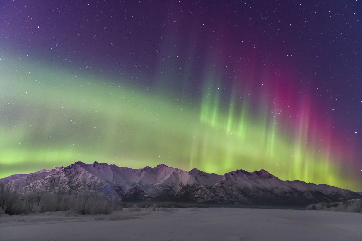 The aurora soars with a hint of red over the Chugach Mountains along the Knik River.