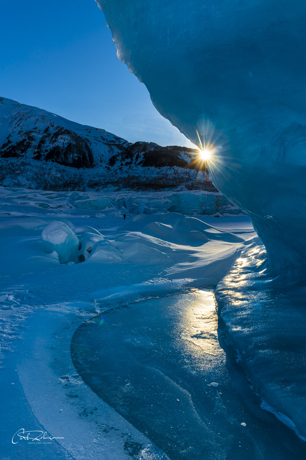 The late afternoon sun peeks from behind a large iceberg suspended in the frozen lake at Spencer Glacier.