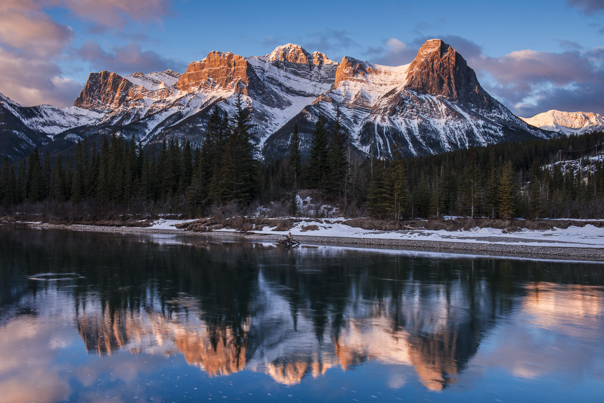 Morning light shines across the peaks and ridges of the Canadian Rockies along the Bow River in Canmore, Alberta, Canada.