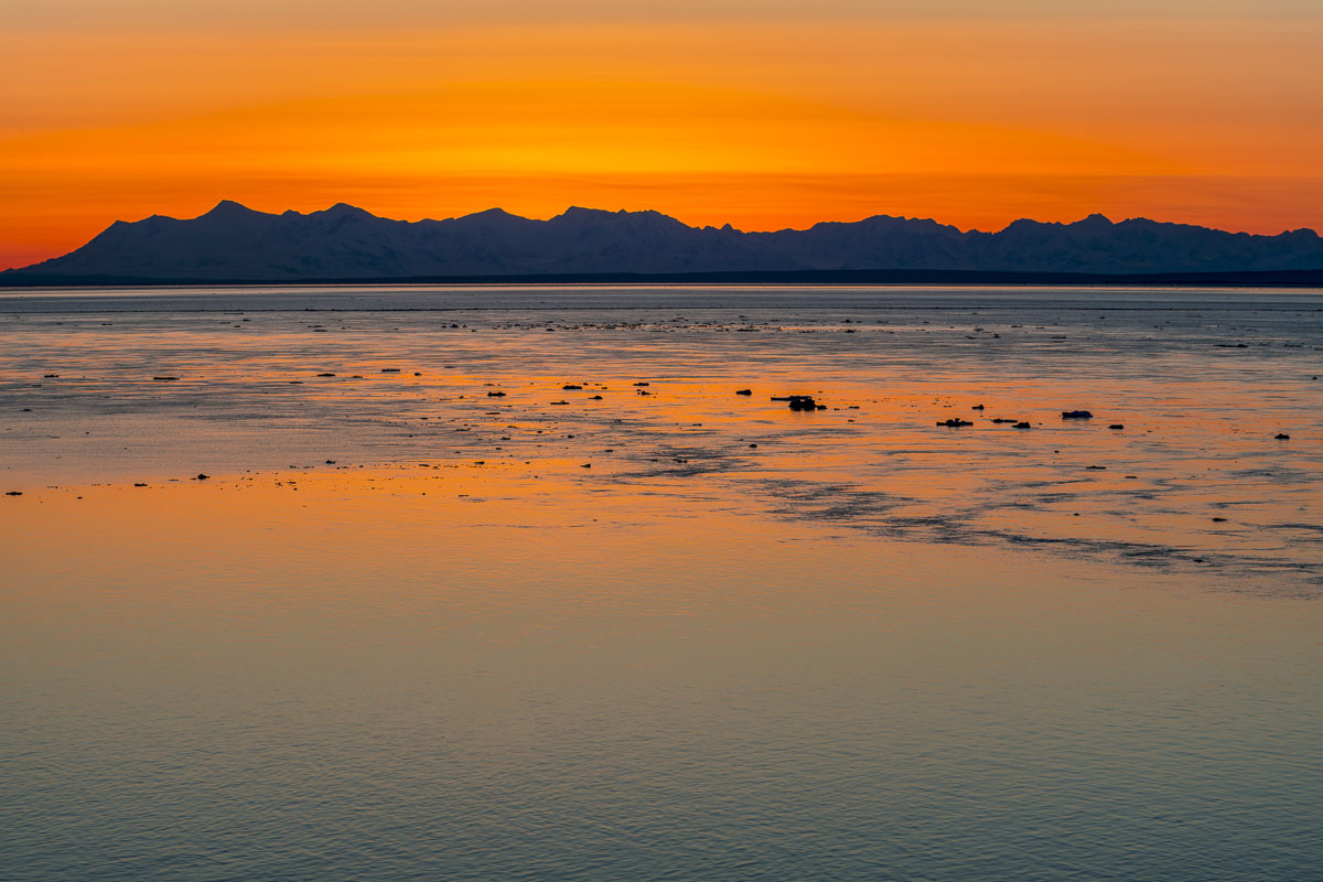 The sky glows gold as the sun sets behing the Tordrillo Mountains on the western side of Cook Inlet. The Tordrillo Mountains...