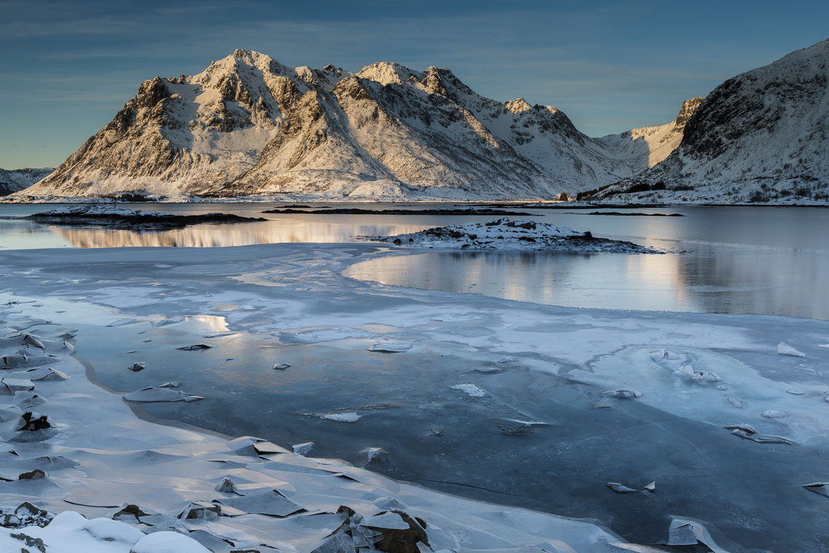 Morning light shines on a mountain and reflects in a partially-frozen Justadpollen, and inlet near the village of Valberg, Lofoten...