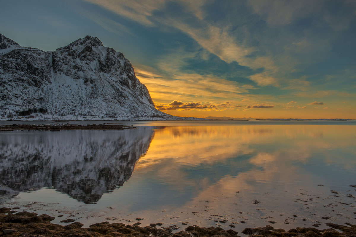 Calm waters in a bay provide reflection of sunrise along a southen coast of the Lofoten Islands.