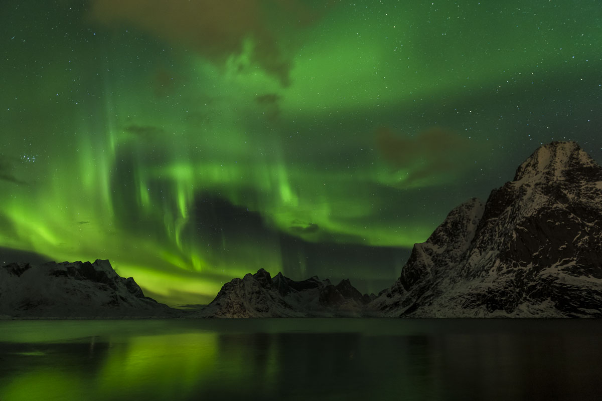 A green aurora borealis fills the sky over a lake in the Lofoten Islands, Norway.