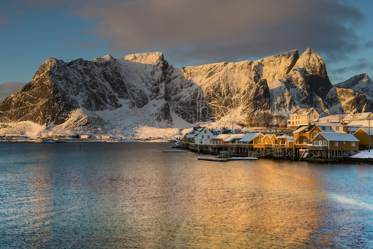 Yellow cabins on Olenilsøya Island with Reinebringen, one of the highest peaks in the Lofoten Islands, in the background.