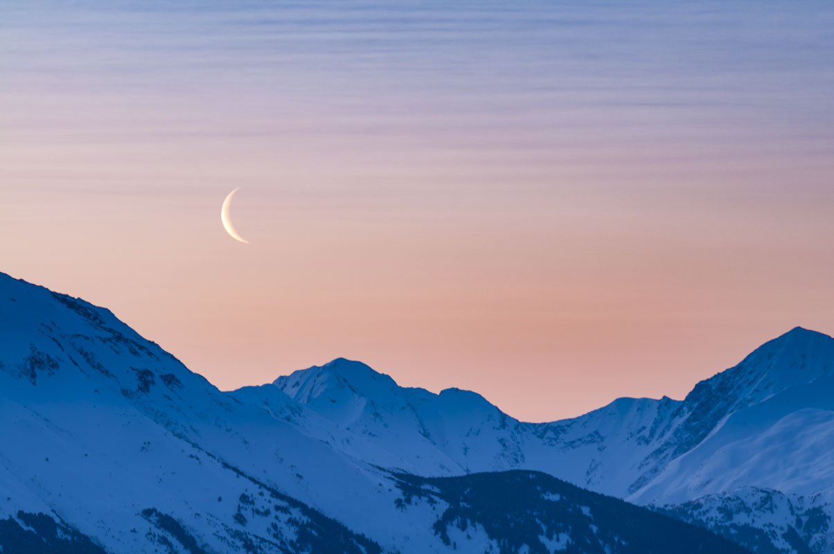 A waning crescent moon rises at dawn in early April over the Kenai Mounatins along the Turnagain Arm, Alaska.