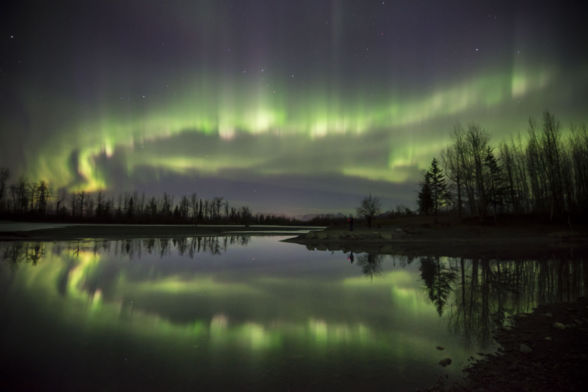 Multiple layers of aurora borealis dance over the Knik River near Palmer, Alaska, during a spring storm. A lone photographer...