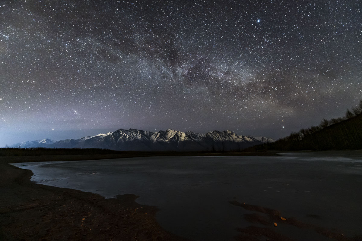 The Milky Way fills the sky over the Chugach Mountains and a frozen Knik River.