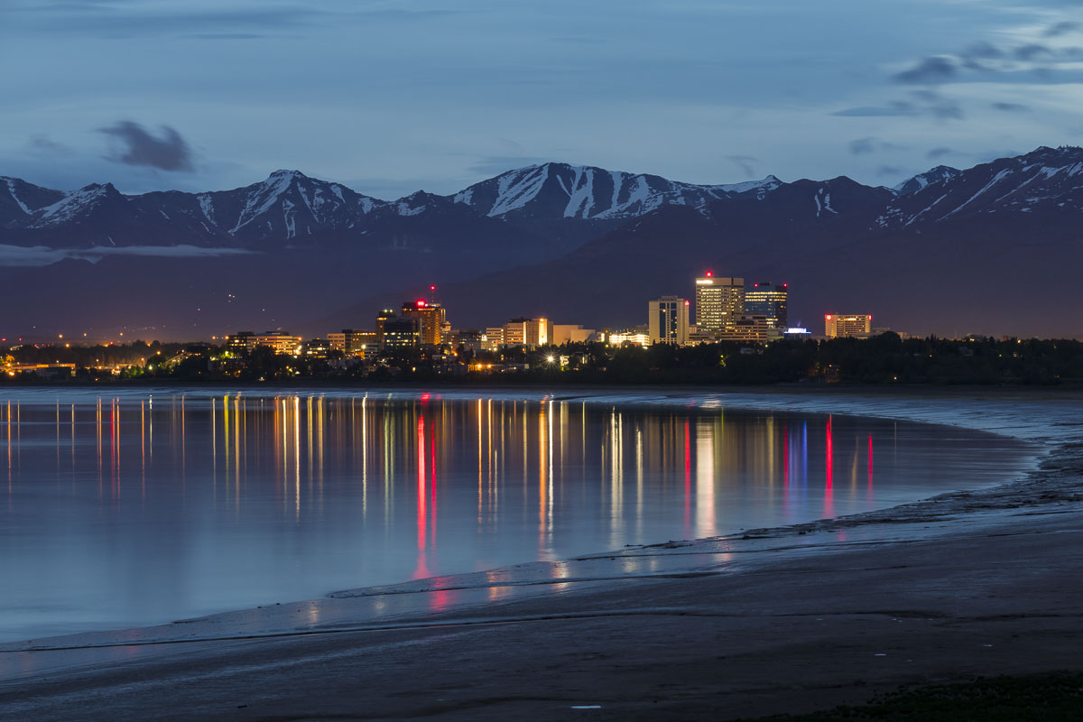 Long reflections of lights from the Anchorage downtown skyline add a rich pop of color to a cloudy summer evening.