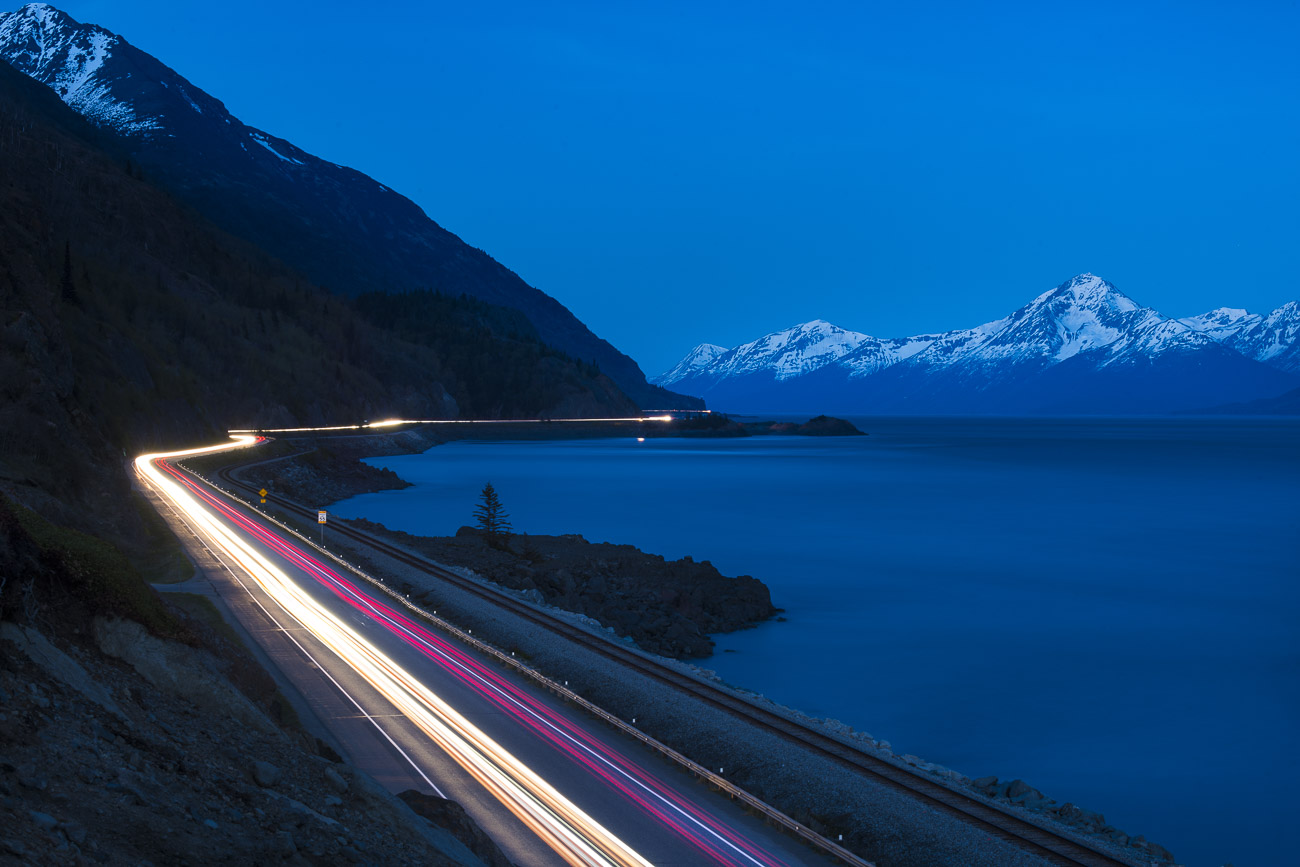 Streaks of headlights and taillights are caught using a long exposure at twilight, as traffic moves up and down the Seward Highway...