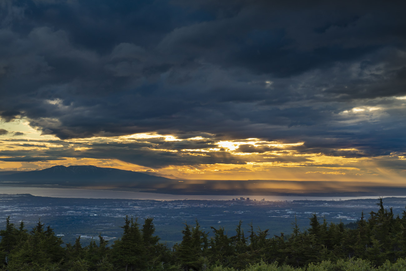 Several shafts of light break through the clouds during a summer storm over Anchorage.
