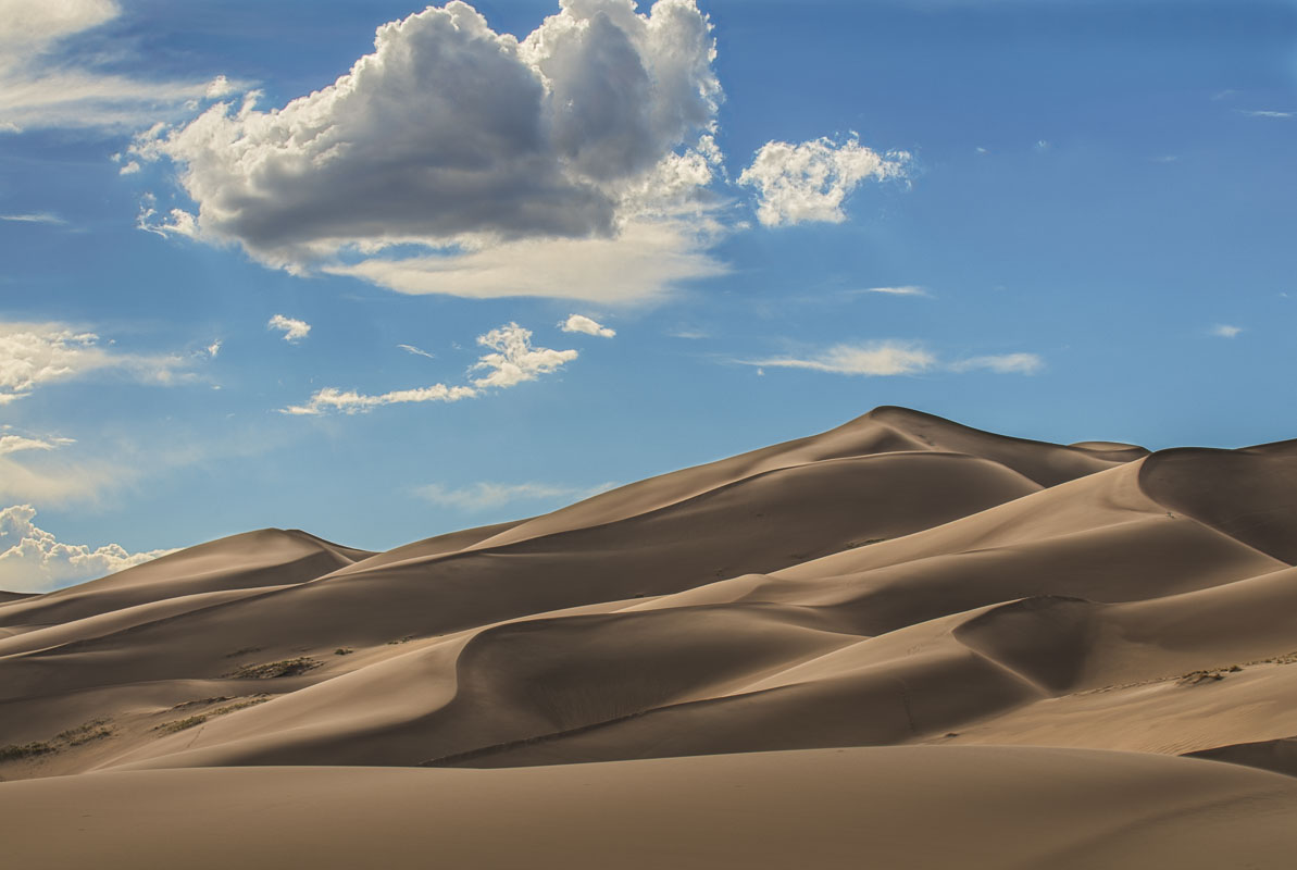 Layers of sand dunes and clouds glow in afternoon sun at Great Sand Dunes National Park & Preserve, Colorado.