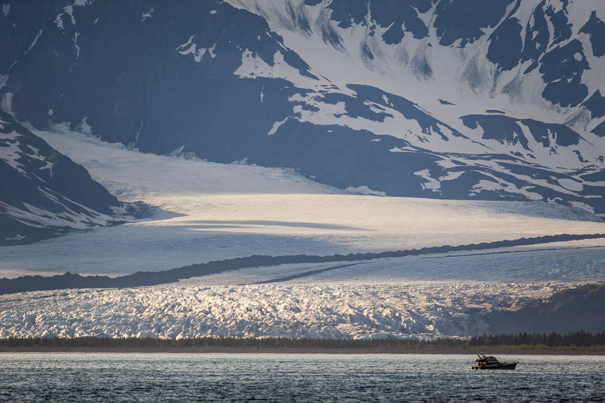 A small boat in the foreground gives a sense of scale to the massive tidewater glacier miles behind it in Kenai Fjords National...