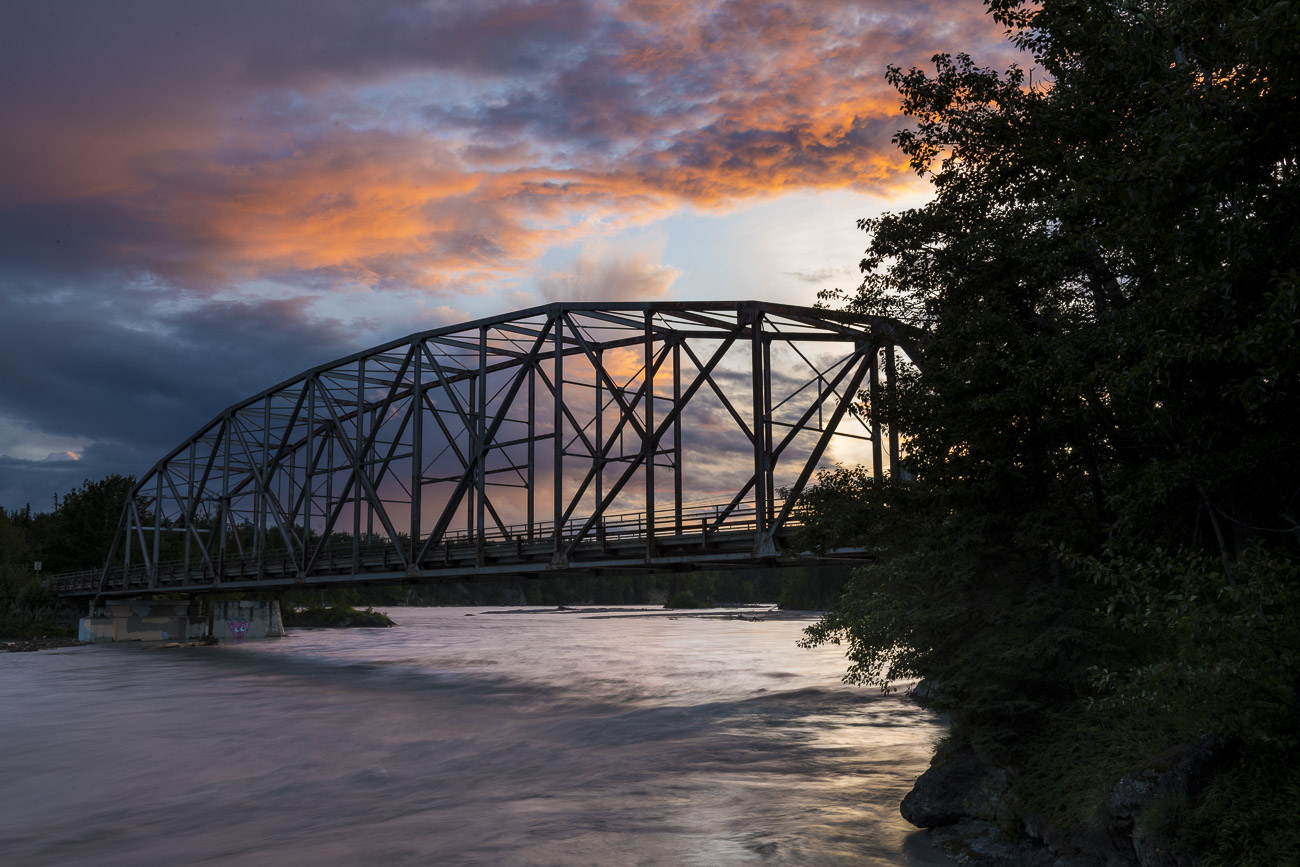 A bridge over the Matanuska River sillhouettes against the colors of sunset on a summer evening.