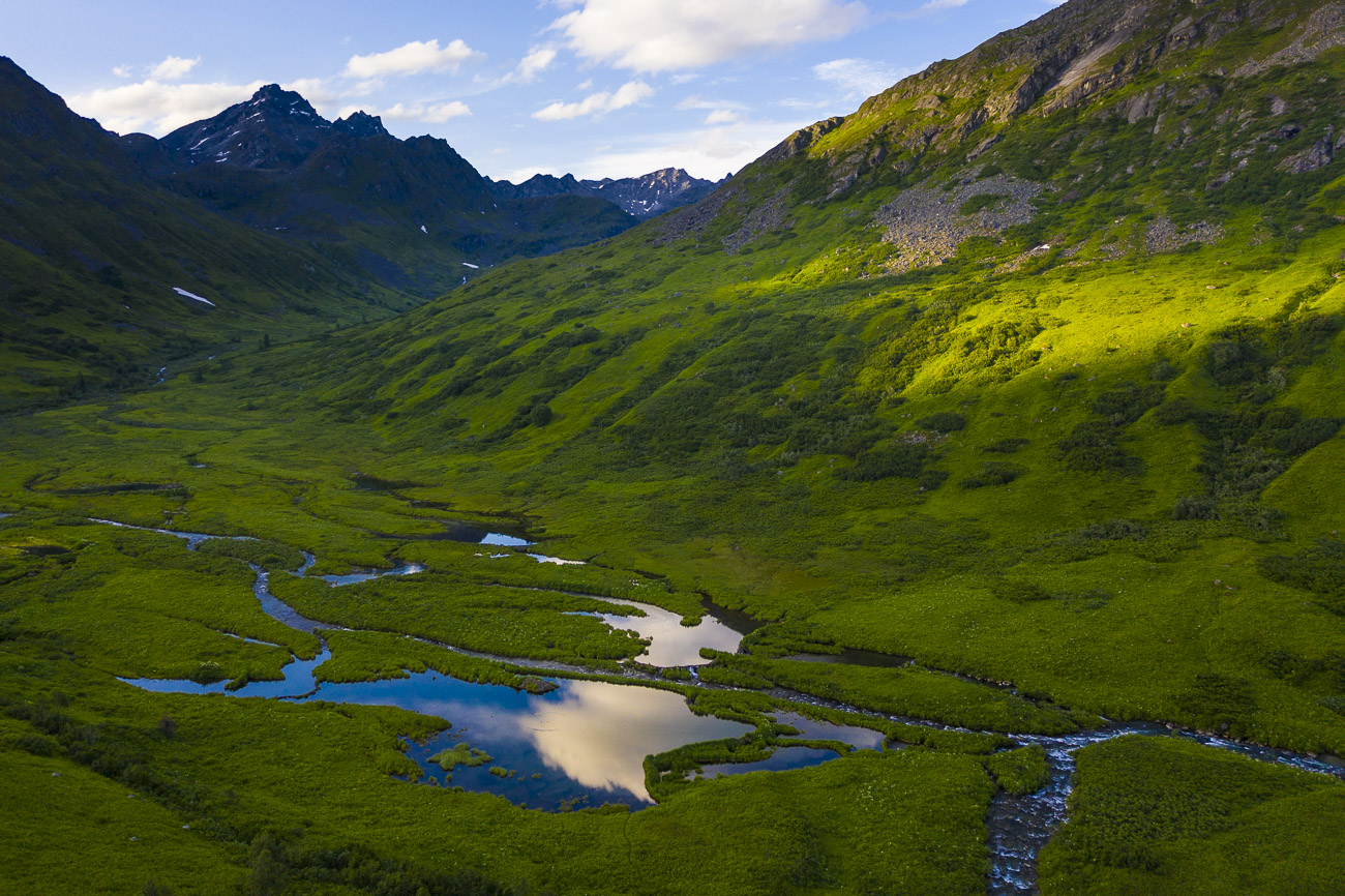 A small shaft of light strikes the side of a mountain in Arcangel Valley in the Hatcher Pass State Recreation Area on a summer...