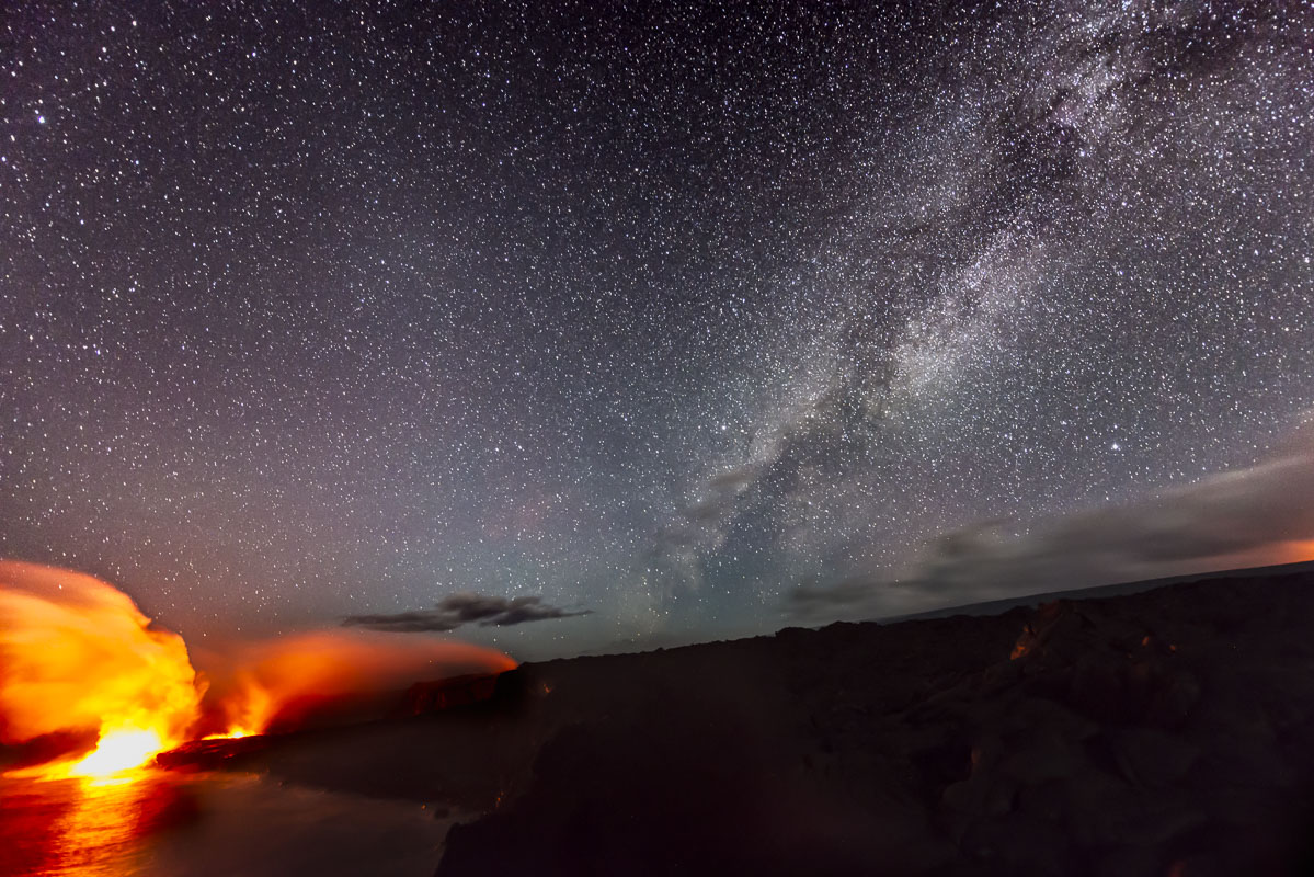 The Milky Way floats in the night sky over lava flowing into the ocean, adding to the continual growth of the land at Hawaii...