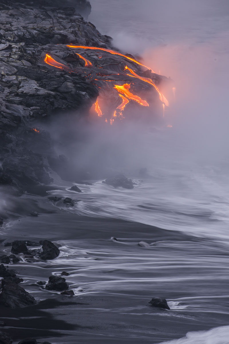 Pre-dawn light starts to brighten the shore as lava continues to flow into the surf at Hawaii Volcanoes National Park.