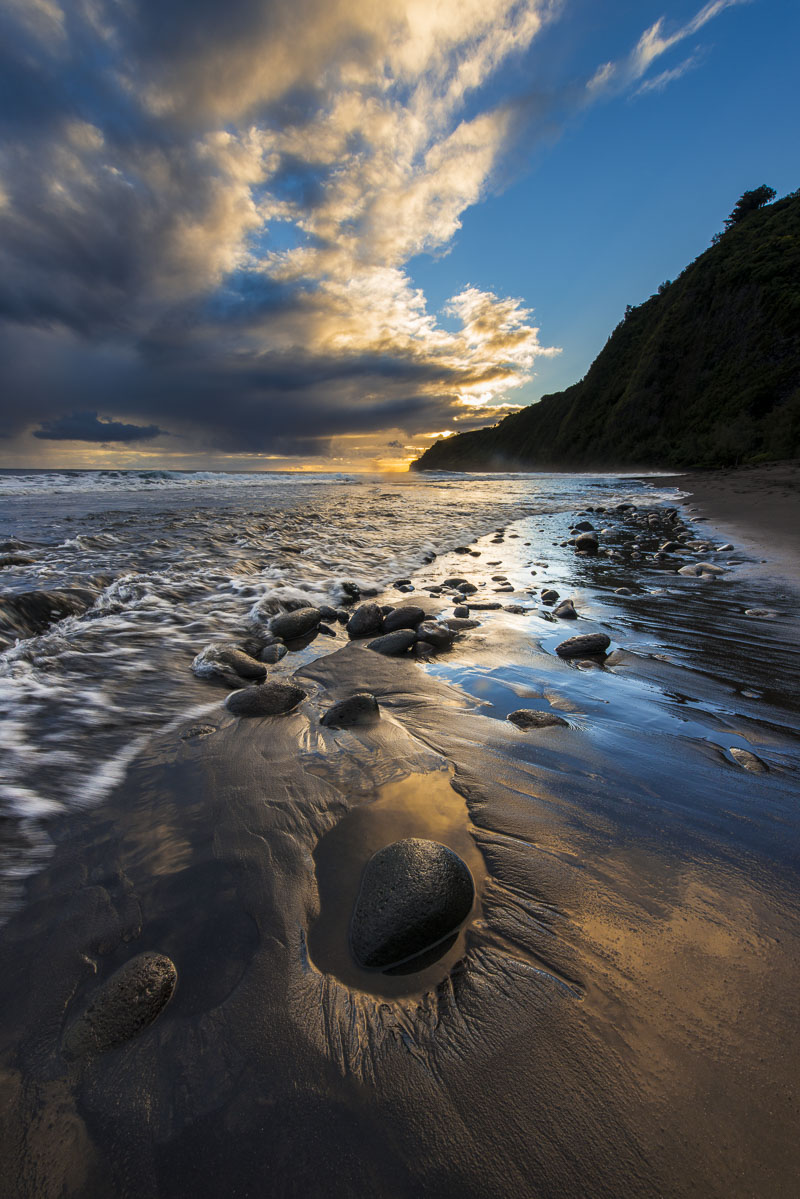 Golden light brushes the edge of clouds and highlights the surf as morning arrives in Waipeo Valley, Hawaii.