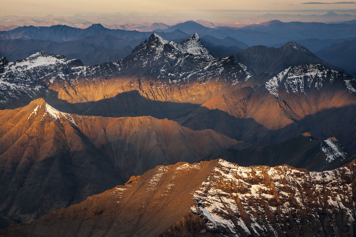 Morning light in autumn shines through clouds to strike ridges in the Brooks Range, as the dual-peaked Mount Boreal stands in...