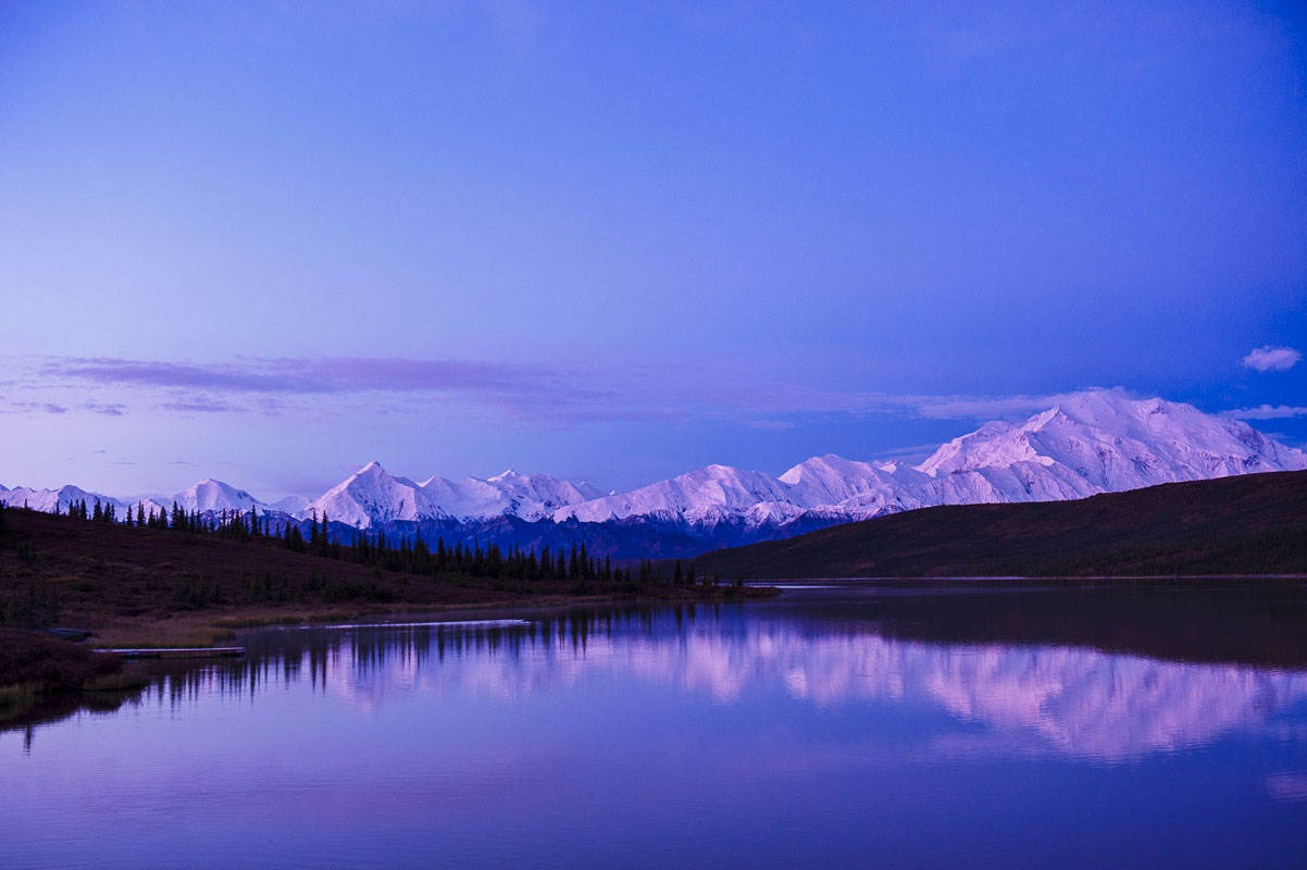 The calm waters of Wonder Lake provide a perfect reflection for Mt. Denali as the colors of dawn glow on its slopes in Denali...