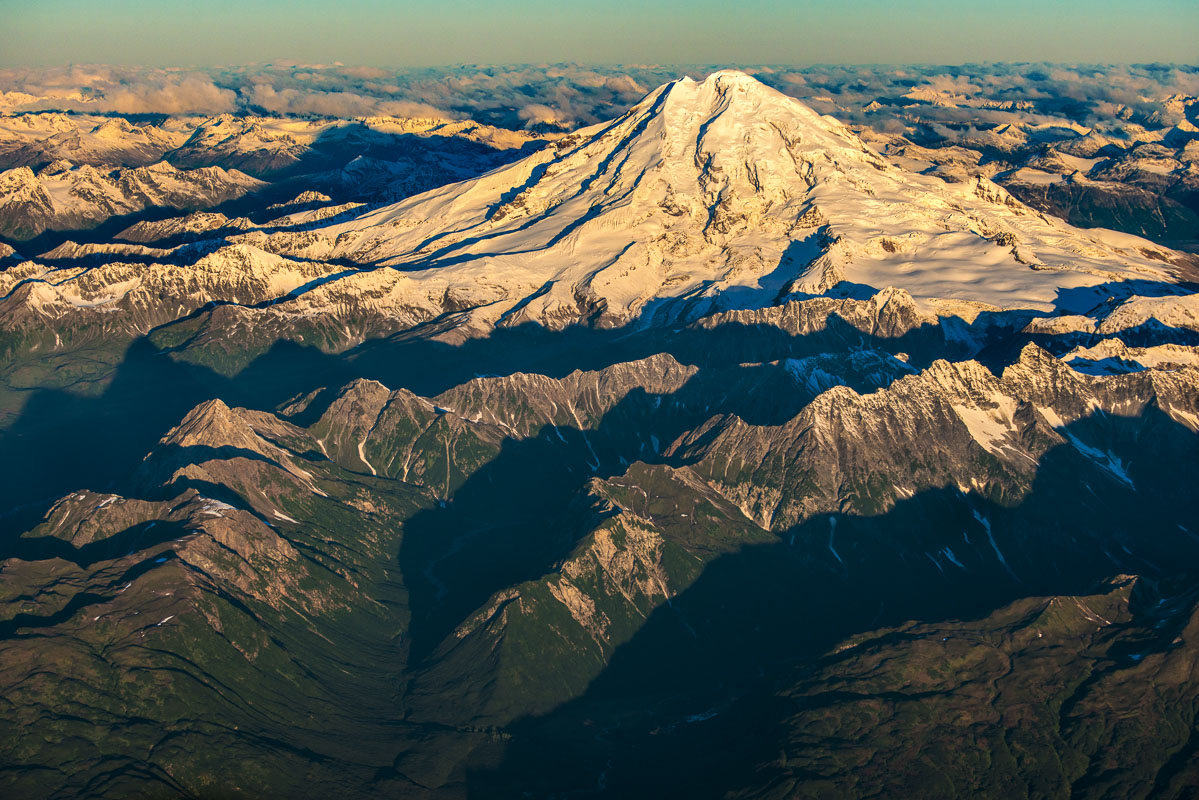 A snow-covered Mt. Redoubt rises above nearby ridges in the Aleutian Range in early light in September.