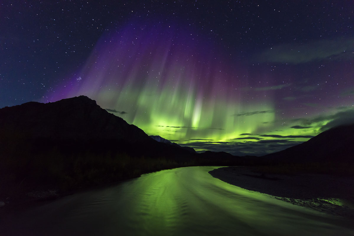 The aurora borealis shines over Mt. Dillon on a moonless night, casting a bright reflection on the Dietrich River.