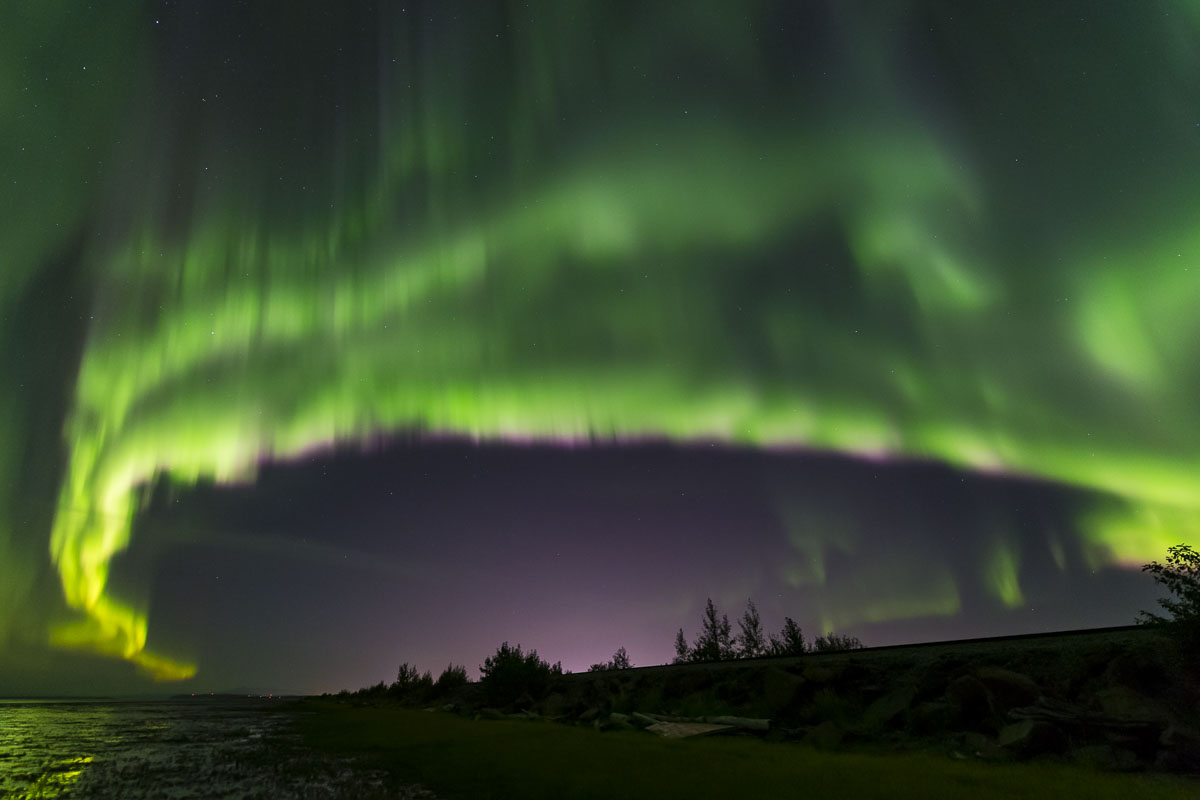 Aurora borealis over coastal Anchorage in early autumn. The glow of the city can bee seen in the middle bottom, showing that...