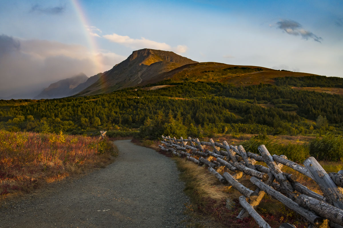 A trail leads toward Flattop Mountain in early autumn as a rainbow splits the sky.