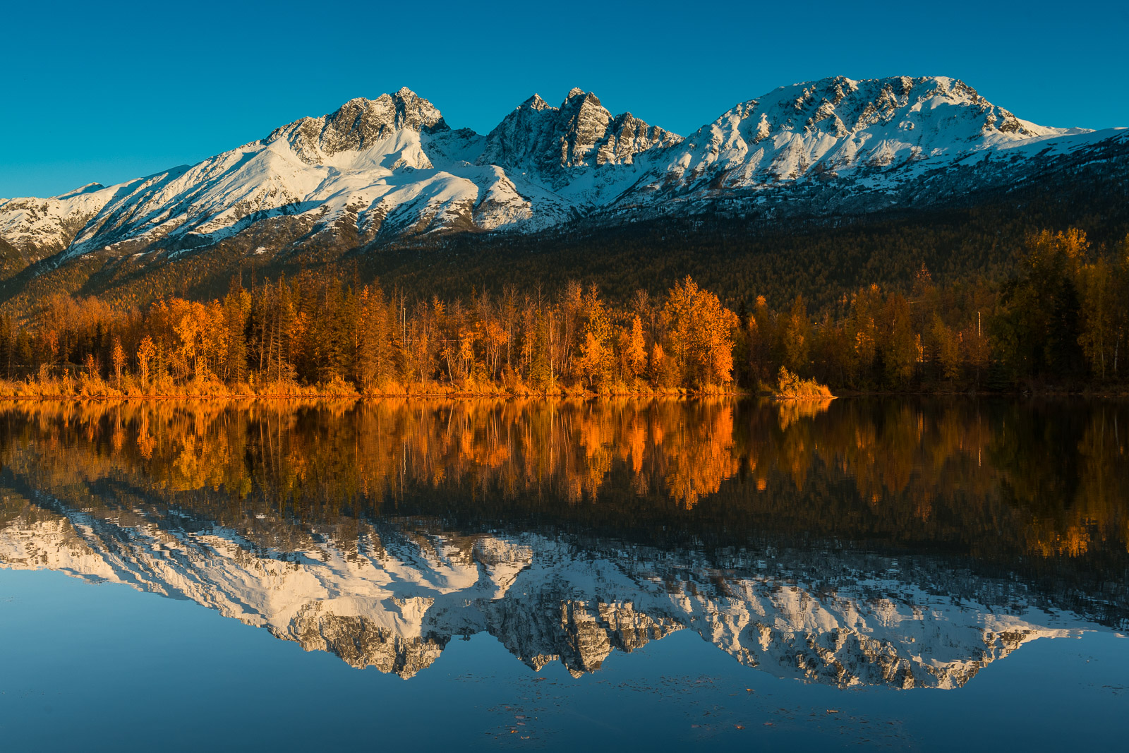 Twin Peaks of the Chugach Mountains reflects in the calm surface of Reflections Lake near the Knik River.