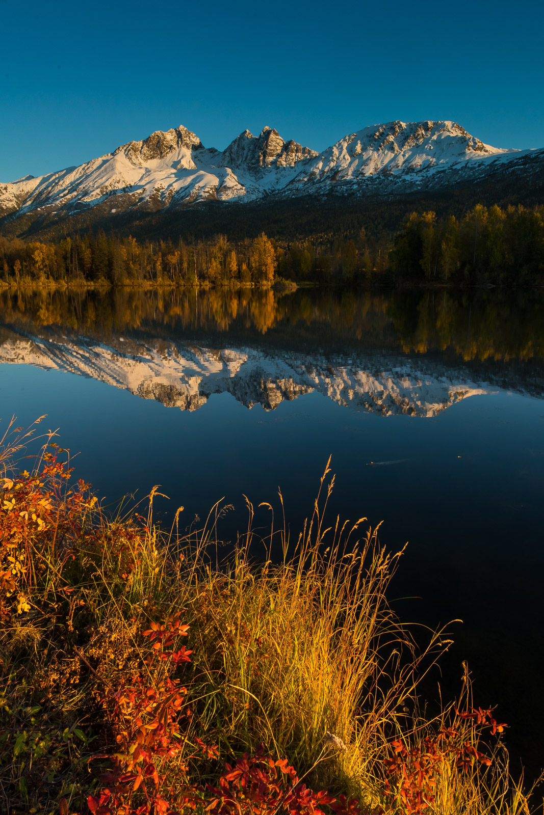 Twin Peaks reflects in the calm surface of Reflections Lake as fall colors decorate the shoreline.