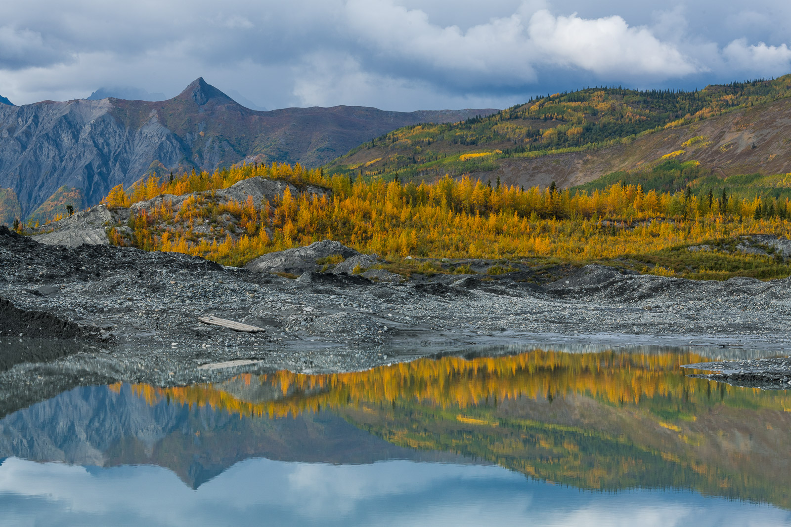 A pool in the moraine of Matanuska Glacier reflects mouhntains and autumn colors.