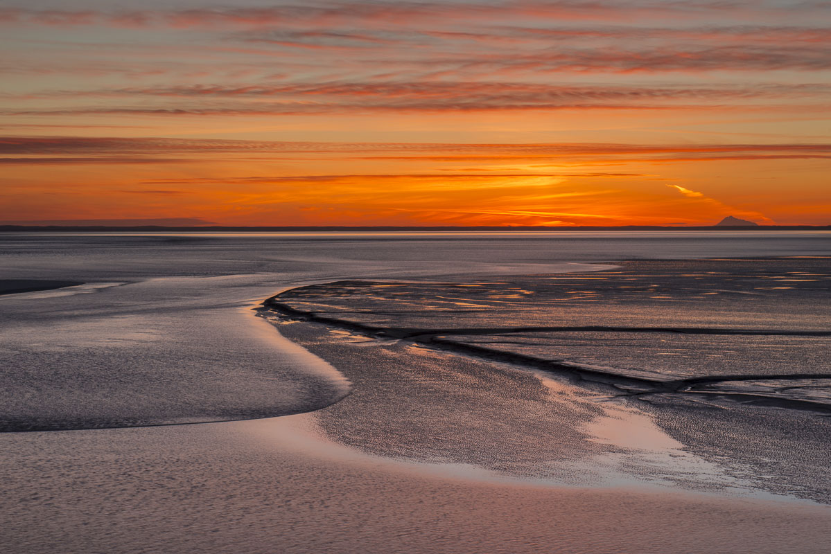 A small bore tide winds its way into the Turnagain Arm south of Anchorage, Alaska, as sun sets behind Mt. Redoubt and the Aluetian...