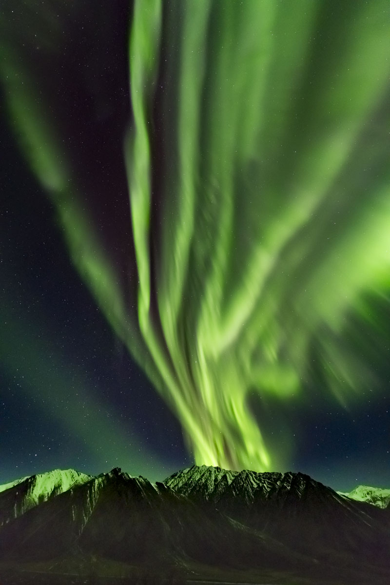 The aurora borealis erupts over the Brooks Range north of Atigun Pass, fanning out across the sky.