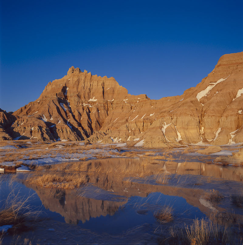 Recent spring snows melt and form a small reflecting pond for a formation in the Cedar Bluffs area of the North Unit, Badlands...