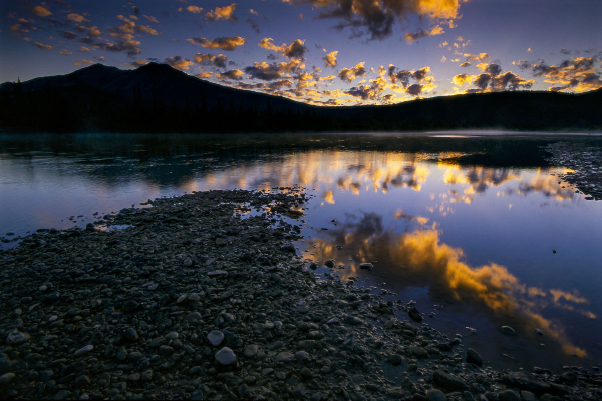 Scattered clouds catch bits of golden light as the sun starts to rise over the Alatna River, Gates of the Arctic National Park...